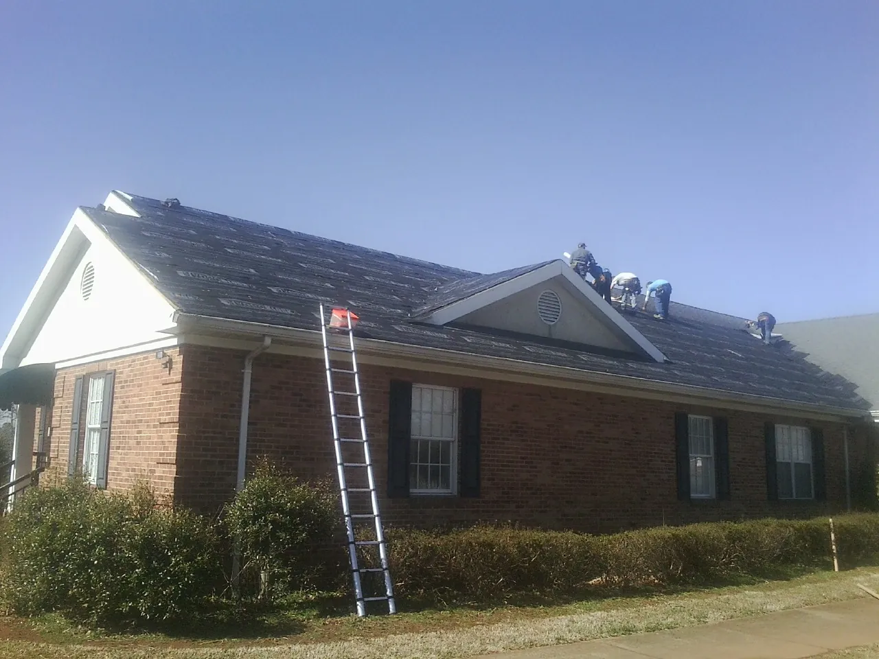 Crew tearing shingles off a brick ranch roof with a ladder set — Metal Roof Repair work by our crew in Middle Point