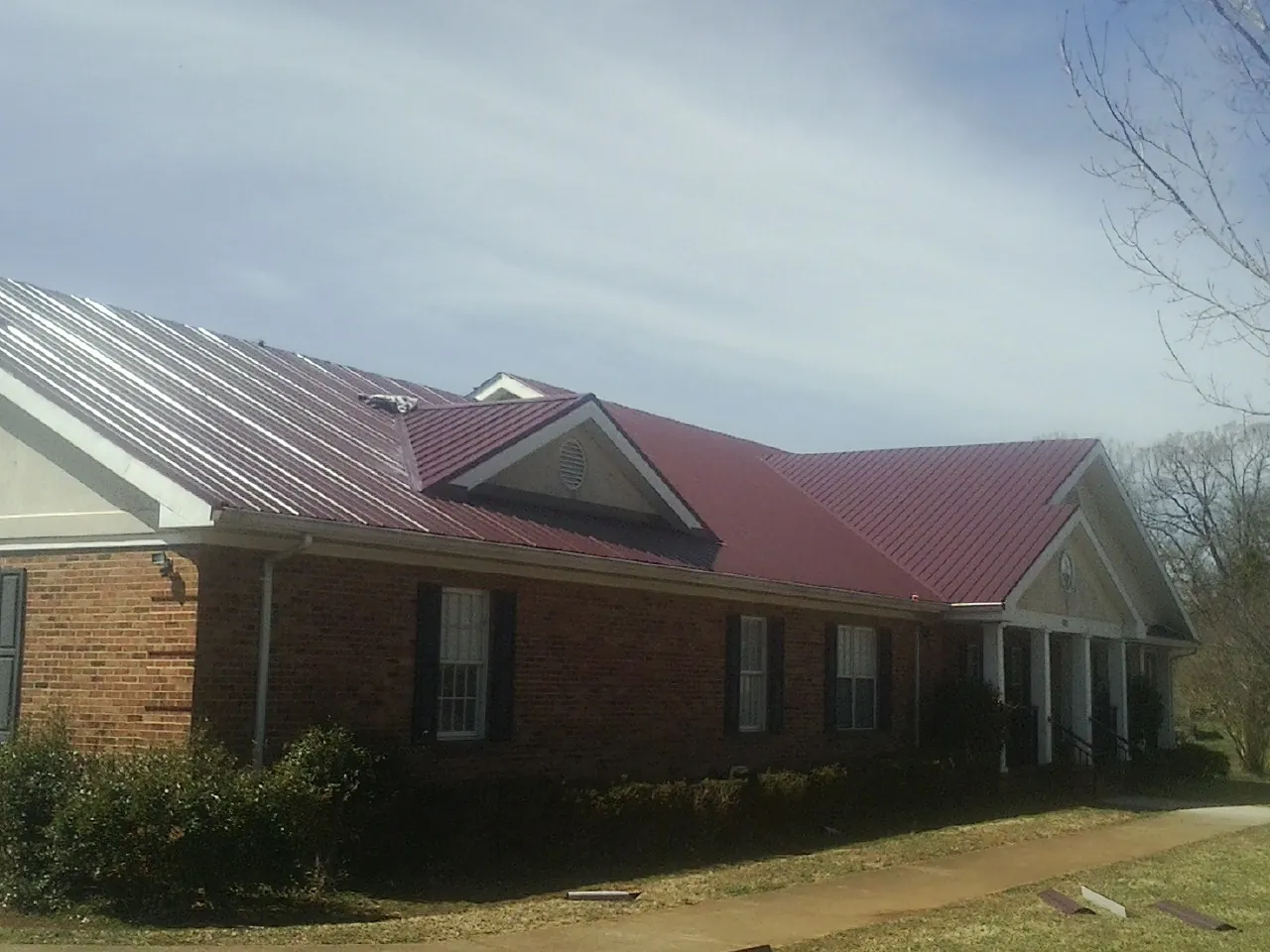Red metal roof with gabled entries on a long brick building, from a Hail Damage Roof Repair job in Middle Point