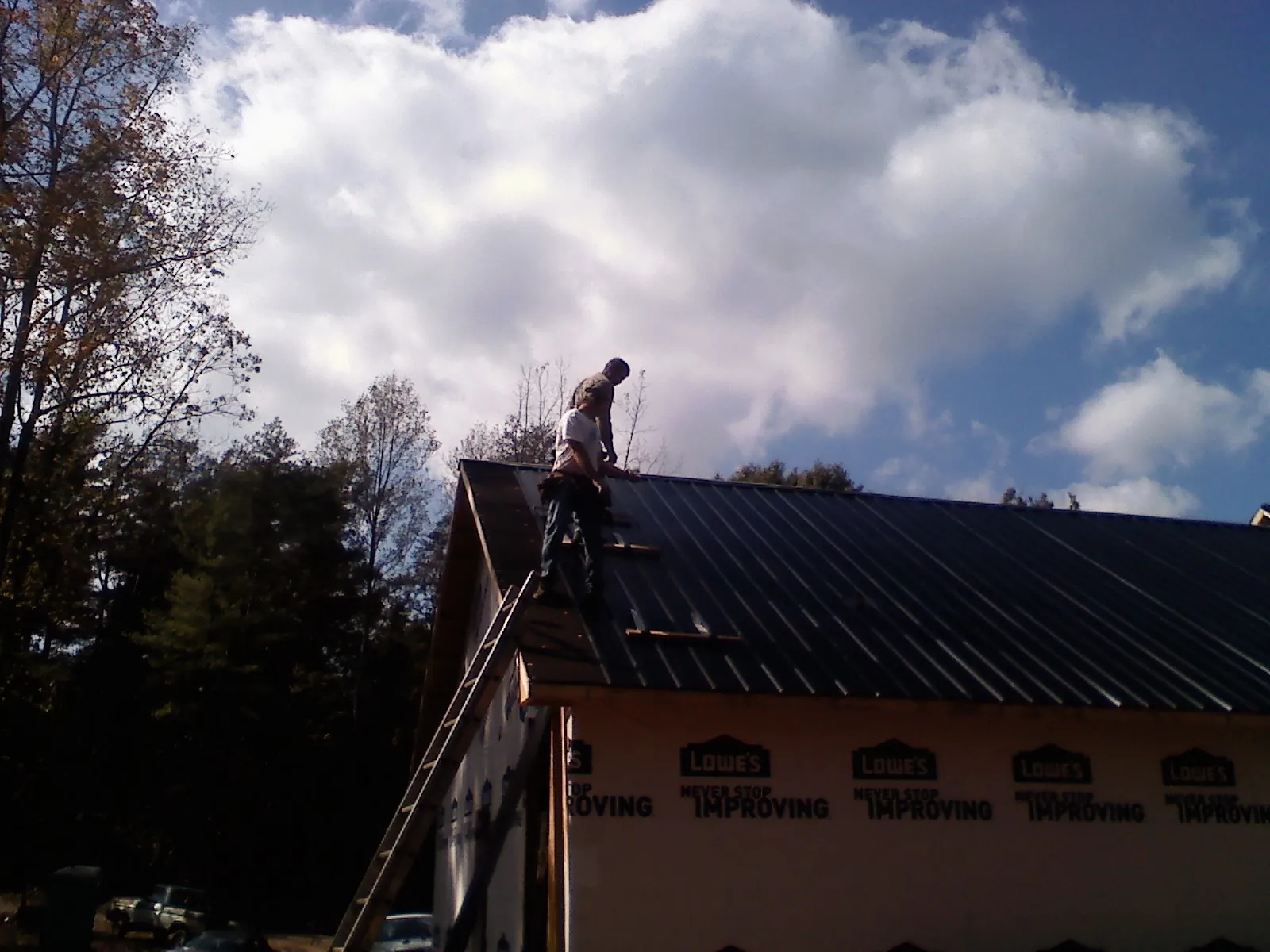 Roofer fastening dark metal panels high against a cloudy sky, from a Roof Inspection job in Middle Point